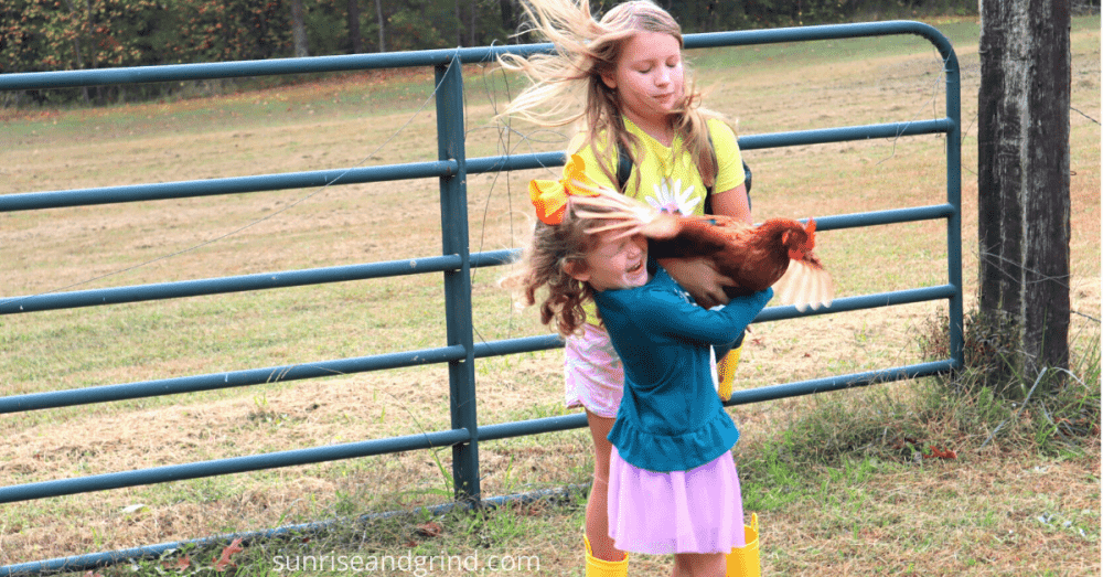 girls holding a chicken while it flaps around on a homestead