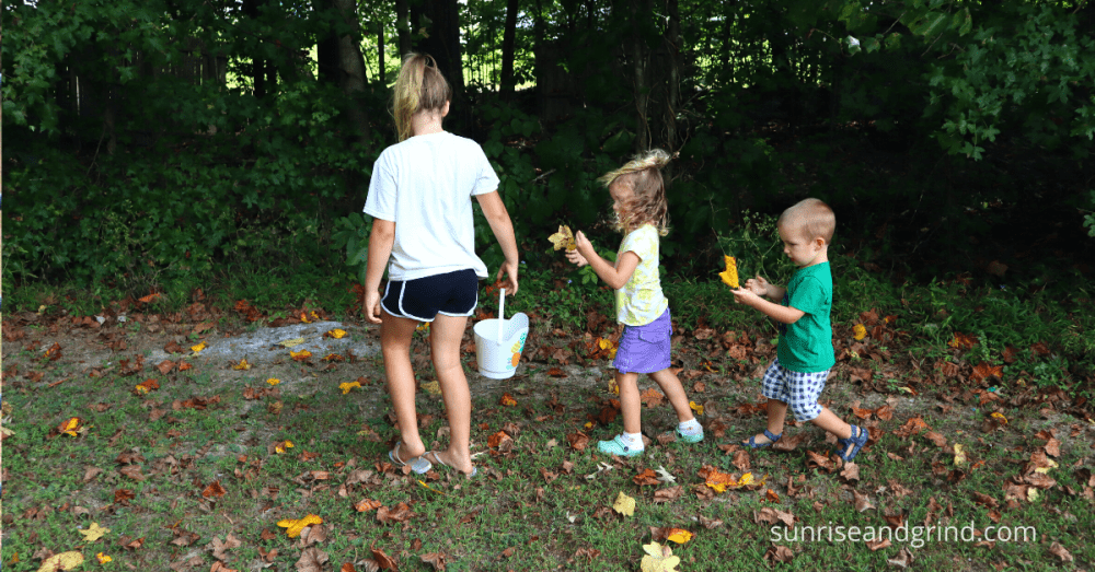 three kids walking around a lawn collecting leaves